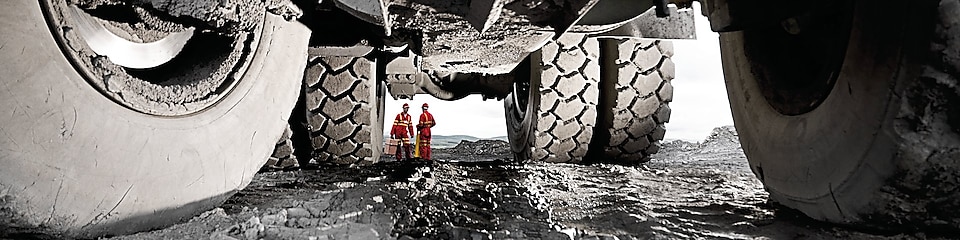 Two men standing under a huge truck. Mining